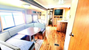 Ein kompaktes Wohnmobil-Interieur mit Essbereich, Sitzgelegenheiten, einer Küchenzeile und einem Fernseher.