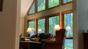 A spacious living room with a large window overlooking a forest, a leather sofa, a wooden coffee table, and two lamps. - Privacy, Fresh Mountain Air, and Thoughtful Hospitality (Stuart)