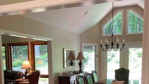 A dining area with a wooden table and chairs, a chandelier, and large windows offering a view of greenery. - Privacy, Fresh Mountain Air, and Thoughtful Hospitality (Stuart)