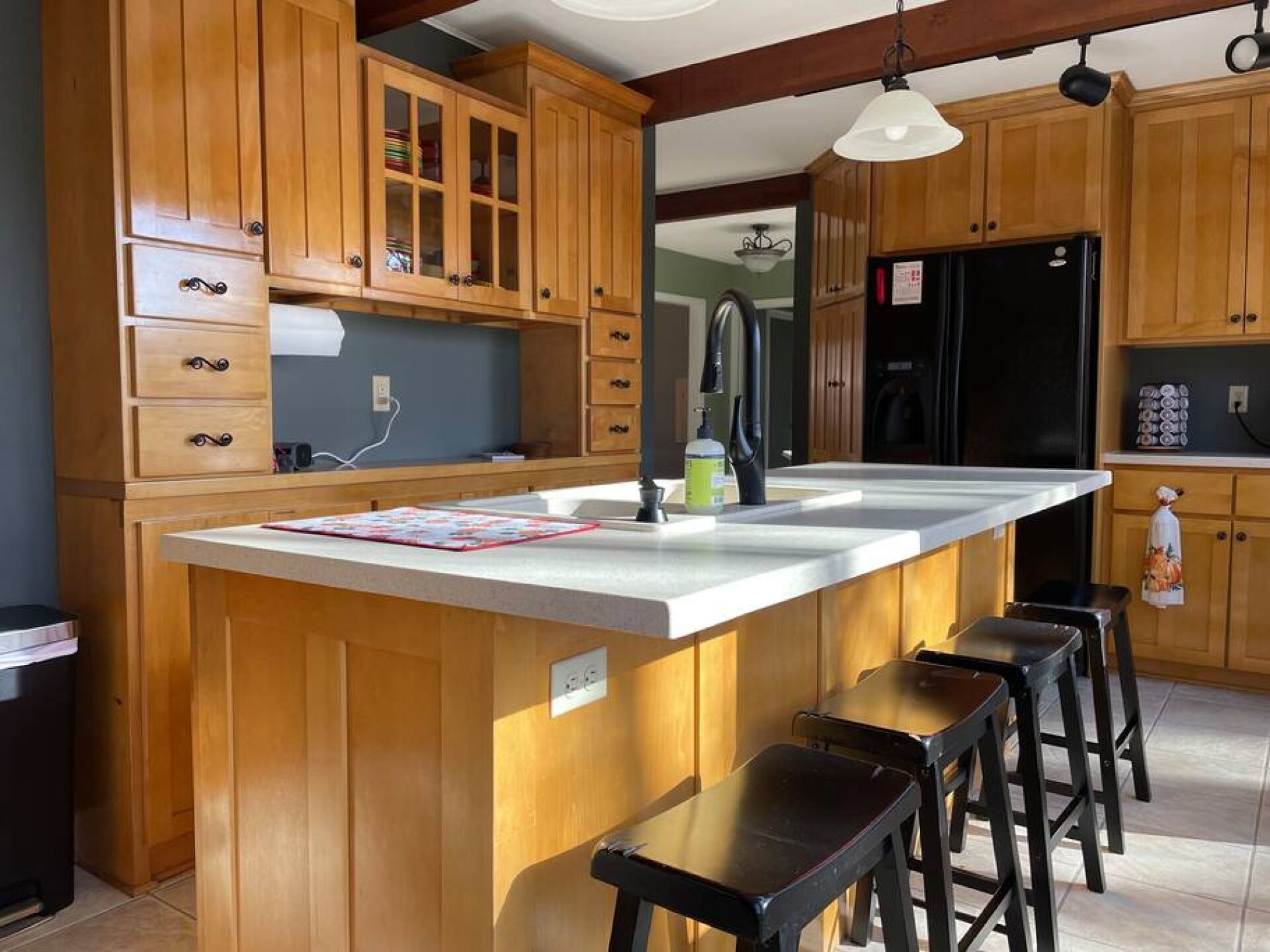 Une cuisine avec des meubles en bois, un grand îlot central doté de tabourets, un réfrigérateur noir et un luminaire suspendu.
