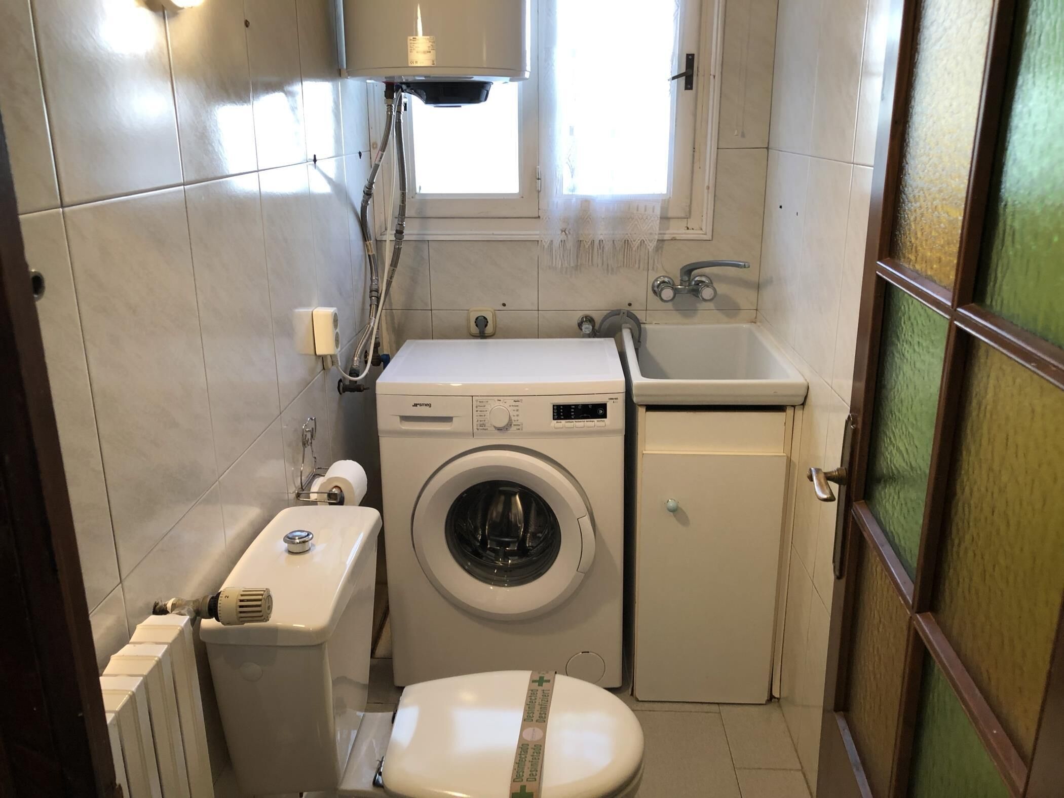 A compact bathroom with a washing machine, toilet, and sink.