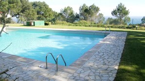 A swimming pool with stone tiles and metal handrails, surrounded by a grassy area and trees. - Apartament Bloc Goya (Begur)