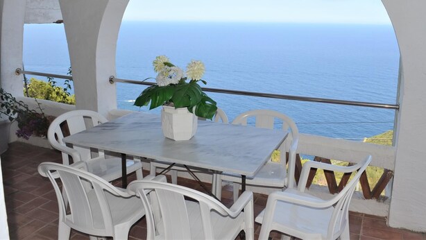 A terrace with a table and chairs, a potted plant, and a view of the sea. - Apartament Bloc Goya (Begur)