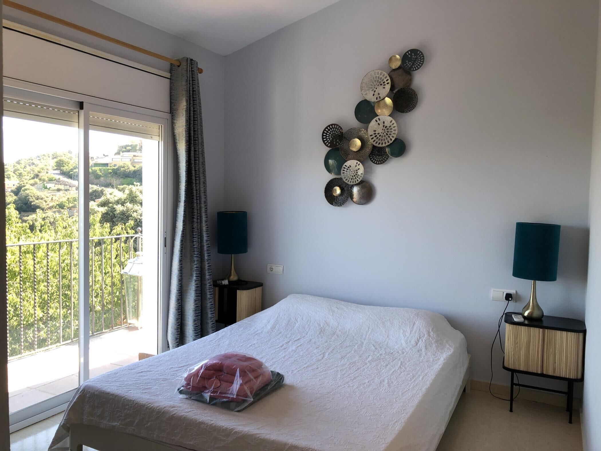 A bedroom with a bed, a view of greenery outside, and a wall decoration.