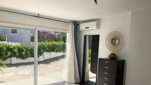 A bedroom with a large sliding glass door leading to a balcony, a bed with a white duvet, a dresser with drawers, and a round mirror on the wall. - Villa Rosa Casa Begur (Begur)