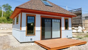 Een klein huis met een schuin dak, grote schuifpuien en een houten terras.