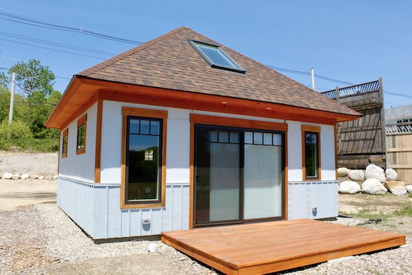 Una casa pequeña con techo inclinado, grandes puertas corredizas de vidrio y una terraza de madera.