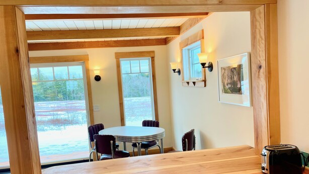 Een eetruimte met een ronde tafel, stoelen en een houten aanrecht met een broodrooster.
