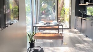 Una cocina moderna con ventanas amplias, un área de comedor con una mesa dispuesta para dos personas y una planta en maceta.