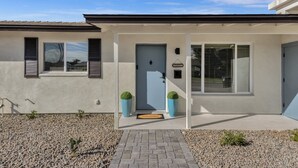 Une maison moderne avec une porte bleue, un paillasson et deux plantes en pot.