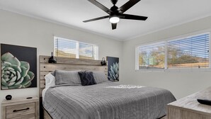 Une chambre à coucher avec un lit, une table de chevet, un bureau et un ventilateur de plafond.