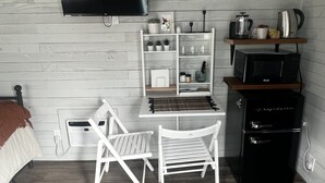 Une chambre de taille modeste comprenant un lit, un bureau avec une chaise, une télévision, une machine à café et un four à micro-ondes.