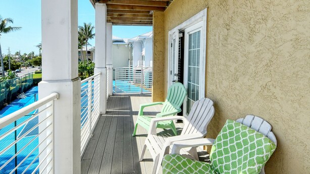 A balcony with a wooden ceiling, a pool, and two green chairs. - Direct beach access! Summer and fall dates still available, call today! (Bradenton Beach)