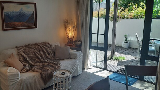 A living room with a sofa, a painting, a lamp, and a view of the outdoors.