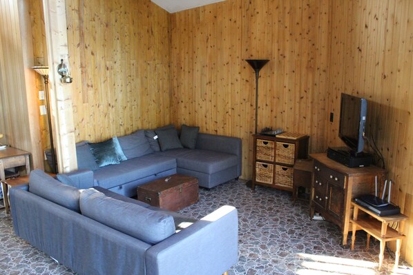 Ein Wohnzimmer mit Ecksofa, Holzboden und Fernseher auf einem Holzschrank.