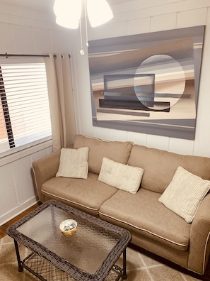 A living room with a beige sofa, a glass coffee table, and a large abstract painting on the wall.