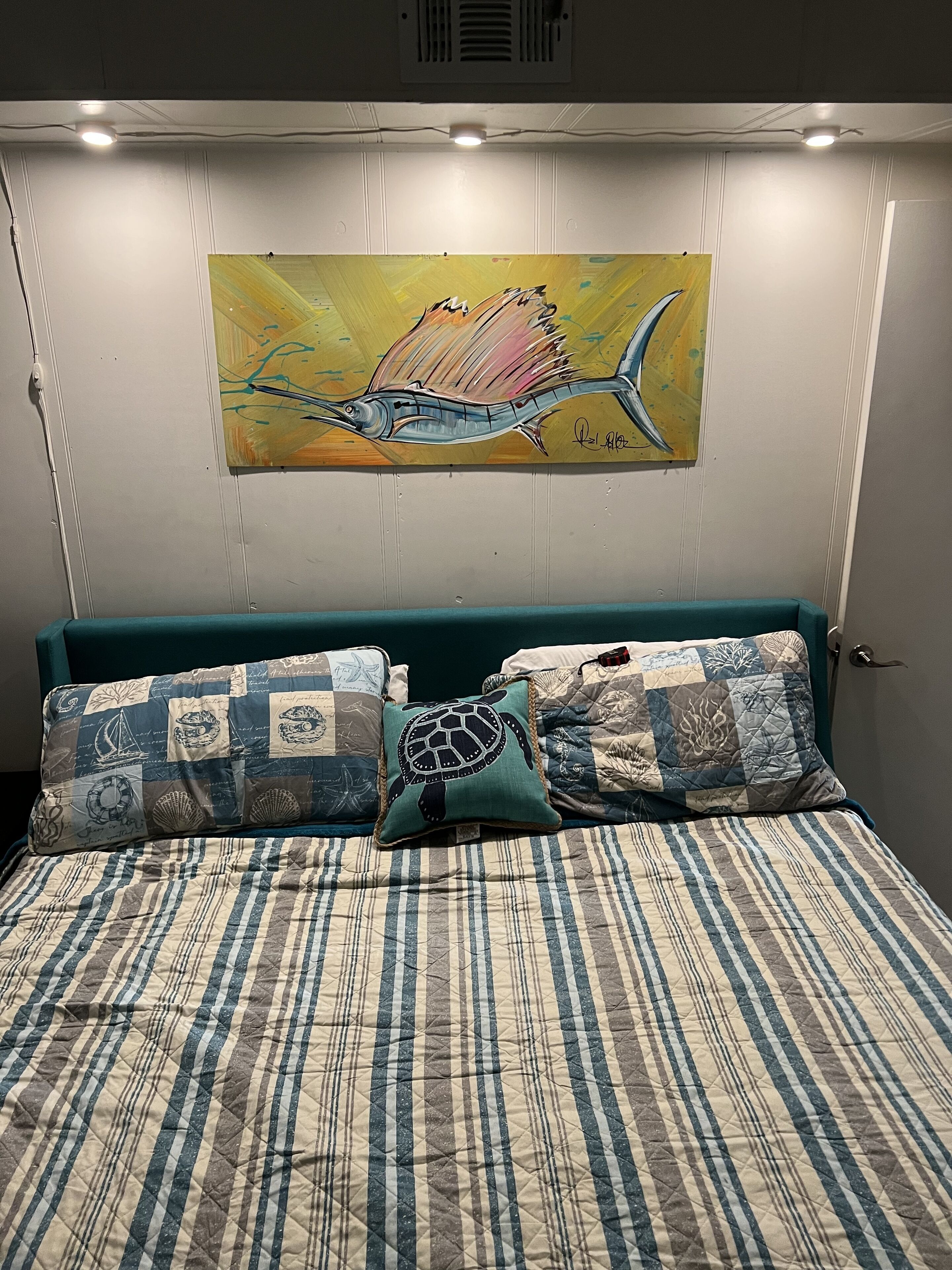 Ein Schlafzimmer mit einem gestreiften Bettbezug, zwei Zierkissen und einem Bild von einem Fisch an der Wand.