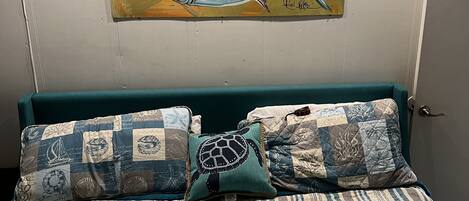 Ein Schlafzimmer mit einem gestreiften Bettbezug, zwei Zierkissen und einem Bild von einem Fisch an der Wand.