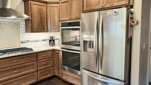 Una cucina con mobili in legno, elettrodomestici in acciaio inossidabile, tra cui frigorifero, forno e microonde, e un piano cottura a gas.