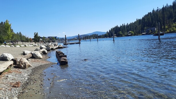 Vista sul lago con un molo di legno che si protende nell'acqua, circondato da rocce e alberi.