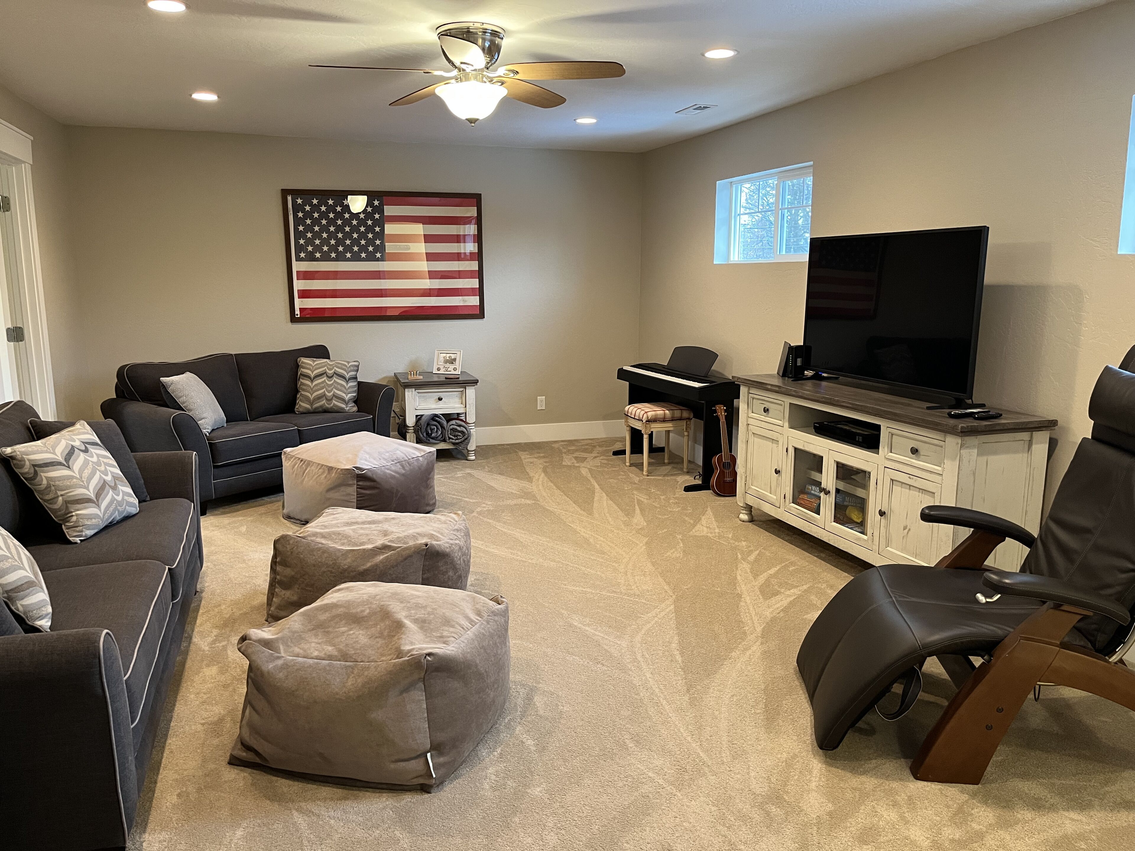 A living room with a sectional sofa, ottomans, a piano, a television, and a flag on the wall.