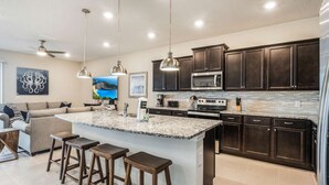 A modern kitchen with dark wood cabinets, a granite island with bar stools, a microwave, and a large island sink.