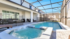 An indoor swimming pool with a hot tub, lounge chairs, and a covered patio area.