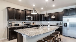 A modern kitchen with dark cabinetry, stainless steel appliances, granite countertops, and pendant lighting.