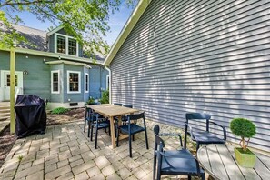 En terrasse med et træbord og stole, grill og et lille pottehegn.
