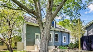 Ein Wohnhaus mit einem großen Baum im Garten, einer überdachten Veranda und einem kleinen Garten.