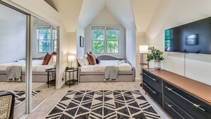 Ein Schlafzimmer mit Bett, Nachttischen, Fernseher, Pflanze und einem geometrischen Teppich.