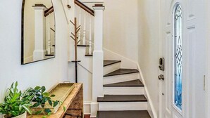 Eine Treppe mit weißen Geländern und einem hölzernen Handlauf, die zu einer Tür mit einer verzierten Glasscheibe führt.