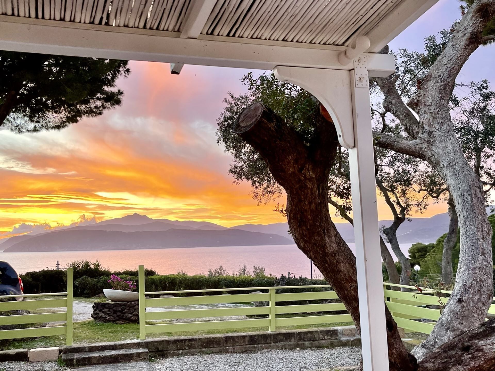Um gazebo com vista para um pôr do sol sobre a água e montanhas.