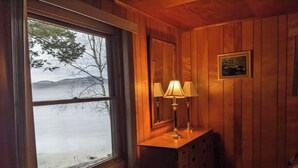 A wooden room with a window overlooking a lake, a wooden dresser with a mirror, and a chair.