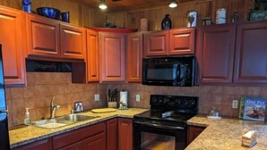 A kitchen with wooden cabinets, a granite countertop, a stainless steel sink, a black microwave, and a black stove.