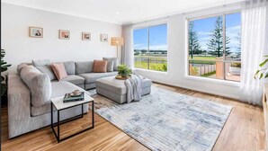 Uma sala de estar moderna com um sofá seccional cinza, uma mesinha de centro e uma grande janela com vista para uma paisagem verde.