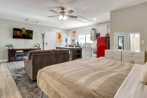 Un dormitorio con cama, ventilador de techo, televisión, kitchenette y baño.