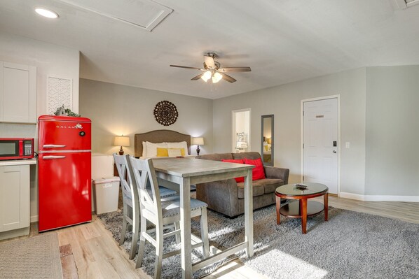 A compact hotel room with a kitchenette, a bed, a ceiling fan, a small table, and a sofa.