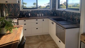 Una cocina moderna con armarios blancos, encimera de madera y vistas al exterior a través de amplios ventanales.