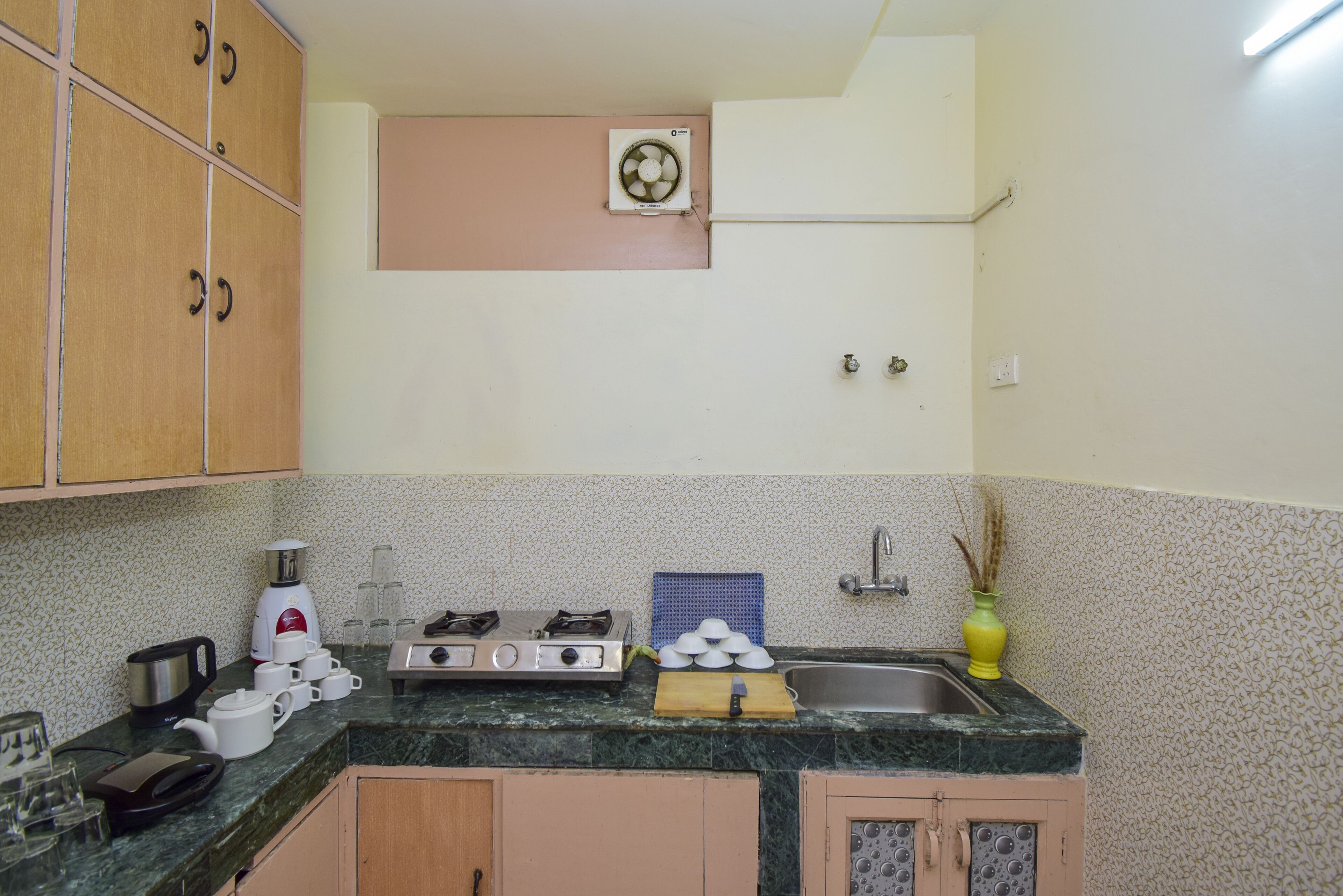 Una cocina con armarios de madera, estufa a gas, pileta y un ventilador de pared.