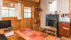 Interior acogedor de una cabaña con paredes de madera, chimenea, mesa de comedor y televisor.