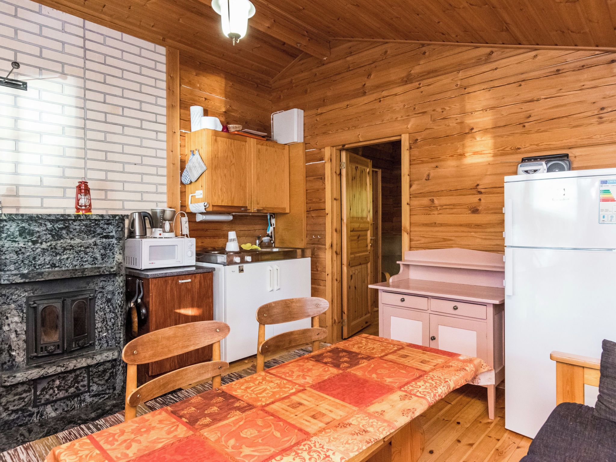 Pieni, käytännöllinen keittiö, jonka seinät ovat puuta, ja jossa on mikroaaltouuni, pesuallas ja jääkaappi.