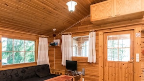 Un acogedor interior de cabaña con techo de madera, un sofá, una mesa de comedor con sillas, un televisor y ventanas amplias con cortinas.