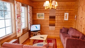 A cozy cabin interior with wooden walls, a sofa, a table, and a television displaying a skier. - Susitupa 6 by Interhome (Salla)