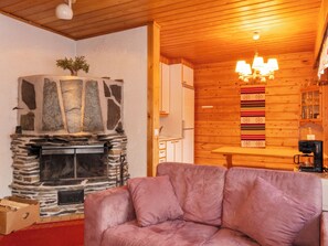 A cozy cabin interior with a stone fireplace, wooden walls, a cushioned seating area, and a kitchen with a coffee machine. - Susitupa 6 by Interhome (Salla)
