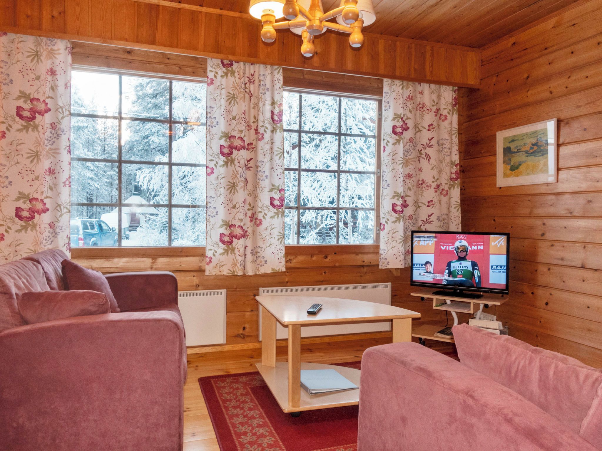 Une pièce chaleureuse aux murs en bois, avec un canapé, une table basse et un téléviseur diffusant un événement sportif.