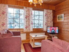 A cozy room with wooden walls, a sofa, a coffee table, and a television displaying a sports event. - Susitupa 6 by Interhome (Salla)