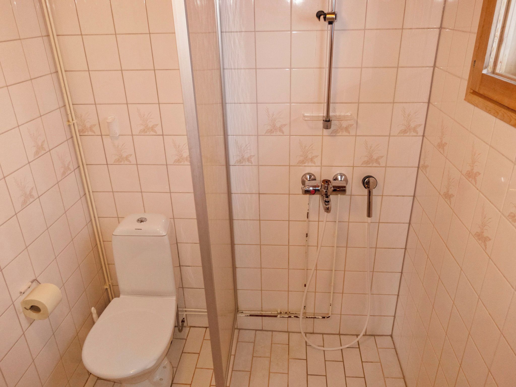 A small bathroom with a toilet, a shower, and a toilet paper roll.