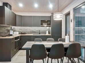 Une cuisine moderne avec des meubles de couleur sombre, un pare-feu en pierre et un coin repas comprenant une table et des chaises.