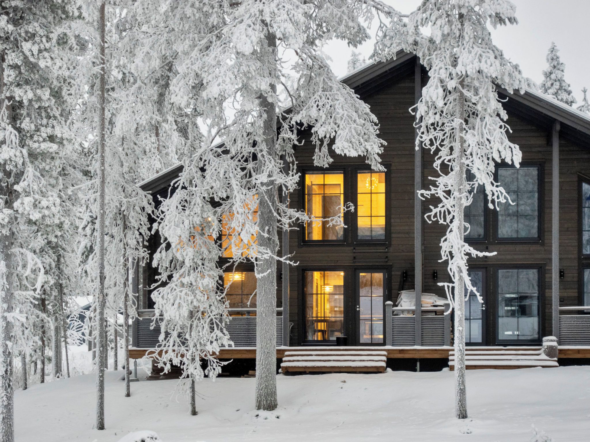 A wooden cabin with multiple windows and a porch, surrounded by snow-covered trees.
